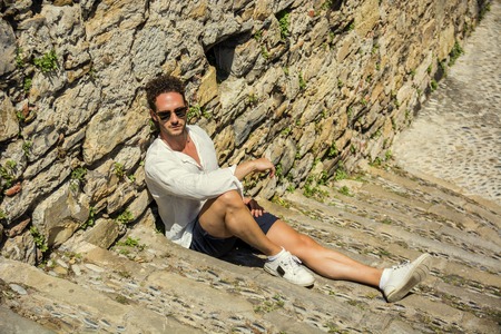 Side view of stylish man in sunglasses sittingon stone stairs and relaxing.の写真素材