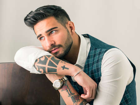 Trendy young man in studio shot wearing elegant vest and white shirt, looking away to a sideの写真素材