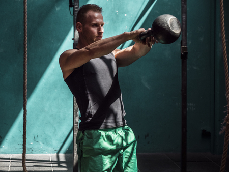 Young man working out with kettlebells in gym, standingの写真素材