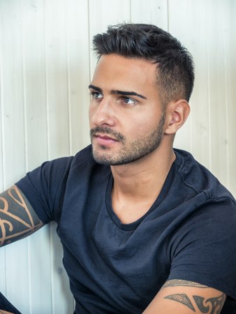 Handsome green eyed young man relaxing at home sitting on his couch, looking away to a sideの写真素材