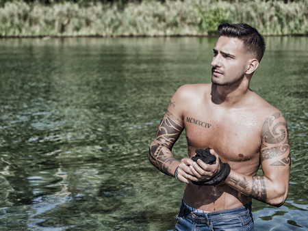 Young handsome tattooed man in wet clothes in the pond.の写真素材