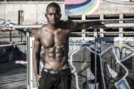 Portrait of a hot black man shirtless in urban environment, walking on metal stairs, looking at...