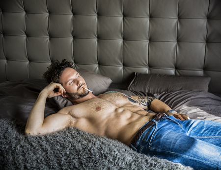Shirtless sexy male model lying alone on his bed in his bedroom, looking at camera with a seductive attitudeの写真素材