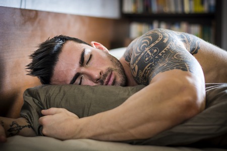 Shirtless muscular sexy male model sleeping alone on bed in his bedroom, restingの写真素材