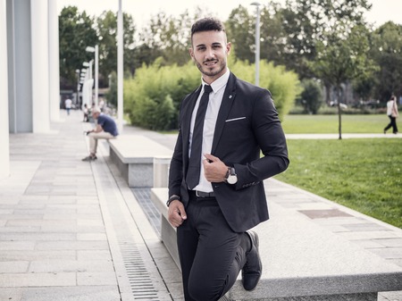 Portrait of stylish young man wearing business suit, standing in modern city settingの写真素材