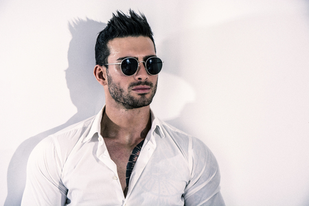 Elegant attractive young man with white shirt, leaning against wall, looking at cameraの写真素材
