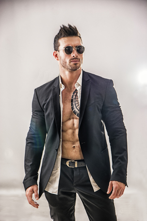 Elegant muscular attractive young man with white shirt open on naked torso, against white wallの写真素材