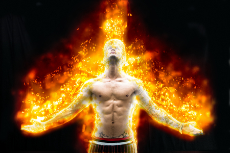 Tattooed muscular man with nude torso holding hands apart and burning in fire on black backgroundの写真素材