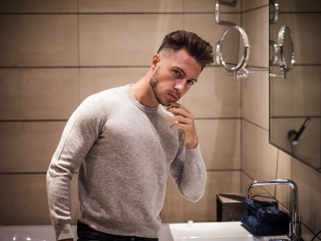 Shirtless handsome young man looking at camera, next to bathroom mirror in the morningの写真素材