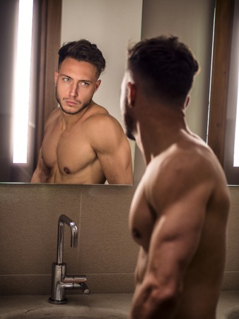 Shirtless handsome young man looking at himself in bathroom mirror in the morningの写真素材