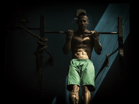 Blond, attractive young man hanging from gym equipment, looking at cameraの写真素材