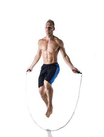 Shirtless muscular young blond man jumping or skipping rope in studio shot, isolated on whiteの写真素材