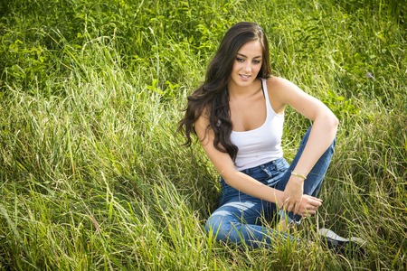Portrait of beautiful smiling girl with long hair sitting on green grass and looking downの写真素材