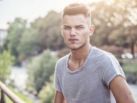 One handsome young man in urban setting in European city park, near a river