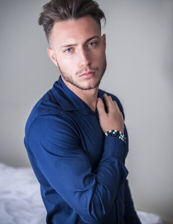 Sexy male model standing in his bedroom, looking at camera with a seductive attitude,, wearing blue elegant shirtの写真素材