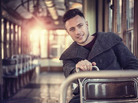 Young handsome man riding on empty tram or old bus in city, wearing winter clothes, sittingの写真素材