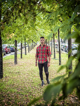One handsome young man in urban setting in modern European city, wearing jeans and red checkered shirtの写真素材