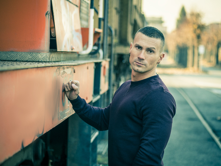 One handsome young man in urban setting in European city, standing, wearing black leather jacket and...
