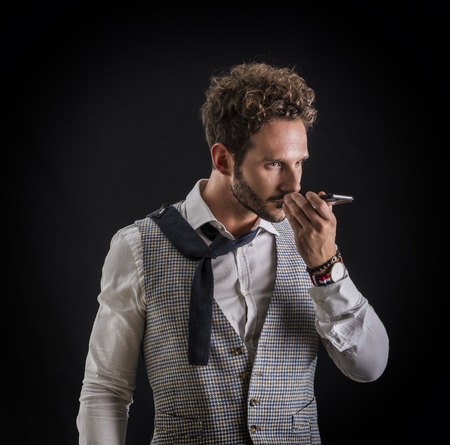 Handsome man sending voice recording or note on cell phone, on black background in studio shot....