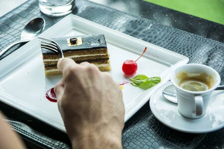 Attractive Young Man Eating Breakfast, Drinking Coffee and Having a Slice of Cakeの写真素材