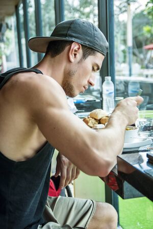 Attractive Young Man Eating Breakfast, Drinking Coffee and Having a Slice of Cakeの写真素材