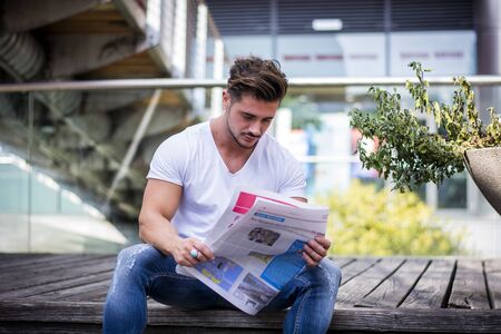 Handsome man reading newspaper outdoor in city setting, sitting on steps