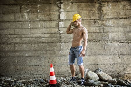 Sexy, muscular construction worker shirtless, working outdoor, wearing blue jeans and yellow hard-hatの写真素材
