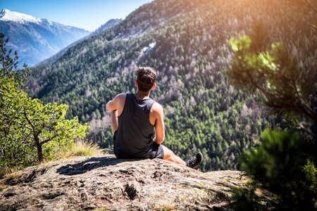 Young unrecognizable man sitting on a rock enjoying the view up the mountain in a sunny dayの写真素材
