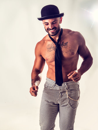 Handsome shirtless muscular man standing on white background, wearing bowler hat and neck-tie on naked torso, smiling happyの写真素材
