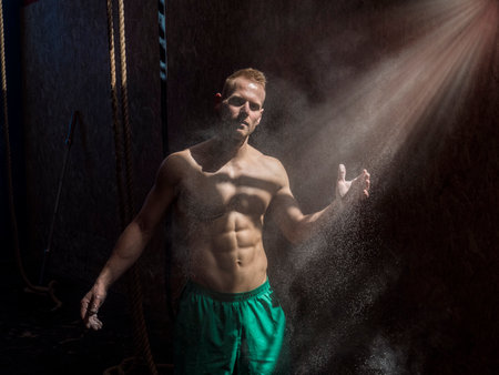 Shirtless man using chalk or magnesium powder in gym, clapping hands and creating cloud