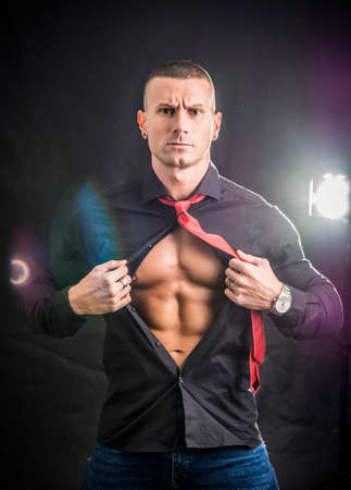 Muscleman opening his shirt revealing muscular torso, on dark backgroundの写真素材