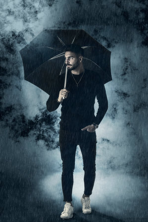 Young man under an umbrella, with rain and fog around at night. Full body shotの写真素材