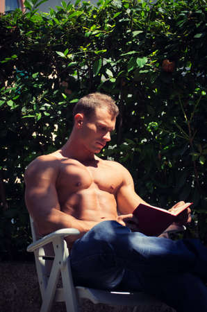 Handsome muscular shirtless young man reading book outside showing muscular pecs and absの写真素材