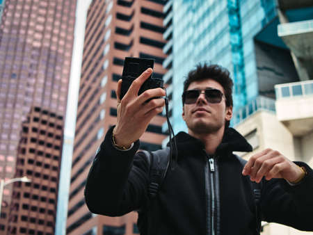 Young man in modern city setting, using smartphoneの写真素材