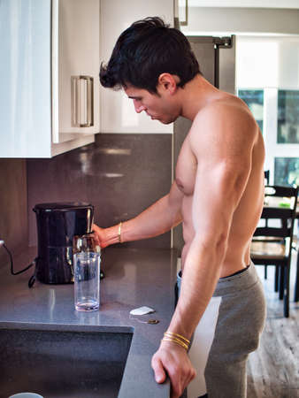 Muscular topless man in kitchen at home making coffeeの写真素材
