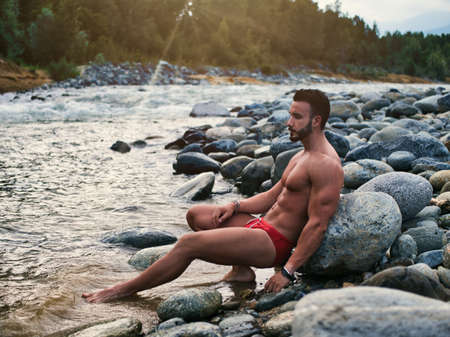 Attractive muscular shirtless young man in nature by riverの写真素材
