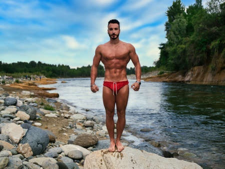 Attractive muscular shirtless young man in nature by riverの写真素材