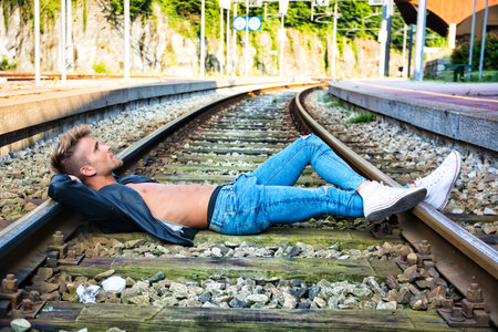 Attractive young man sitting on railroad, during the dayの写真素材