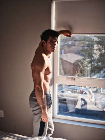 Sexy young man standing shirtless by curtainsの写真素材