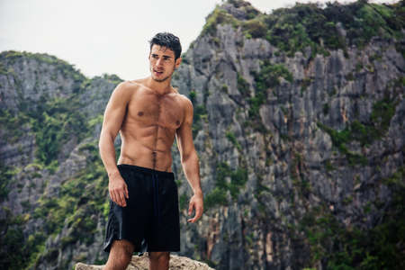 Young man standing shirtless, hills in background