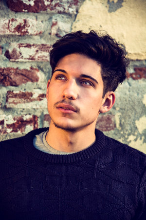 Portrait of handsome young man leaning on old brick wall