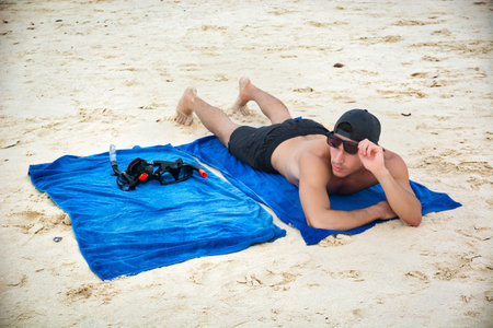 Half body shot of a handsome young man laying on a tropical beach in Thailandの写真素材