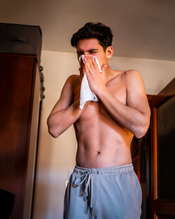 Attractive Shirtless Young Man with Cold or Allergies Blowing Nose into Tissueの写真素材