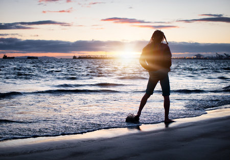 Traveler standing on wet sandy beach at sunset