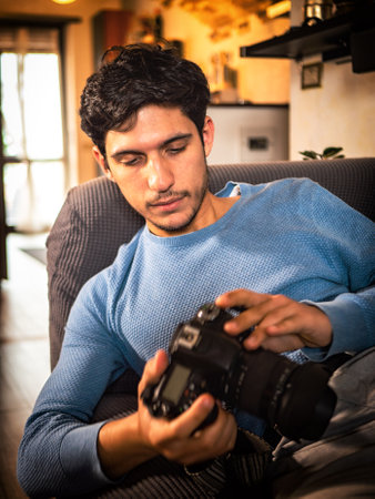 Young male photographer holding and looking at his photocamera