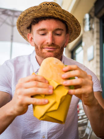 Photo of a man in a straw hat enjoying a sandwich outdoorの写真素材