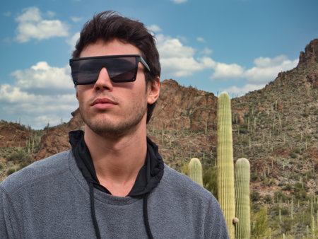 Photo of a stylish man posing in front of a tall cactus wearing sunglassesの写真素材