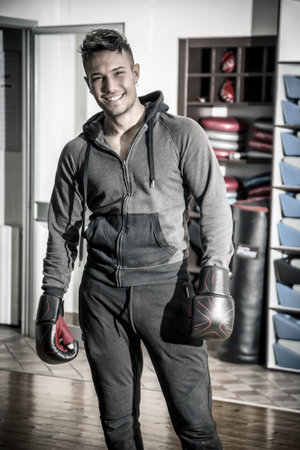 Photo of a young man with a fierce look, ready for a boxing match, holding a boxing glove in a gymの写真素材