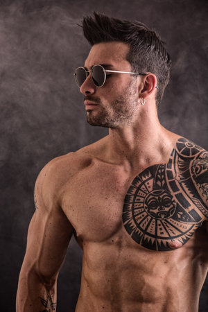 Photo of a muscular man showcasing a sun tattoo on his chestの写真素材