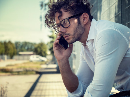 Photo of a man talking on a cell phone while sitting on a ledgeの写真素材